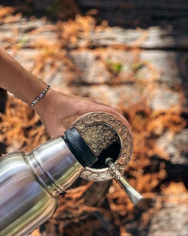 Termo cebando un mate de alpaca labrado sobre fondo cálido